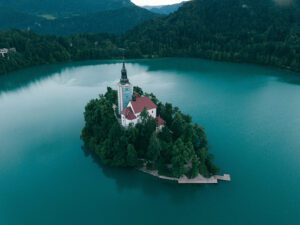 Fotografía aérea de una pequeña isla en medio de un lago rodeado de montañas con una casa