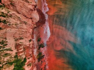 Fotografía aérea de un acantilado y la orilla de una playa con tonos rojizos