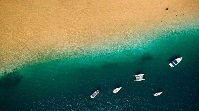 Fotografía aérea de la orilla de una playa con gente tumbada y barcos