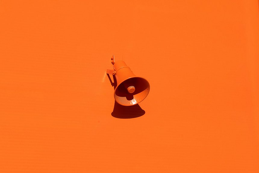 Fotografía artística con un megáfono en el centro de color naranja y el fondo del mismo color