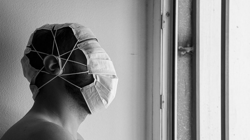 Fotografía artística conceptual de Hombre encerrado en casa, mirando por la ventana, con muchas mascarillas por la cabeza
